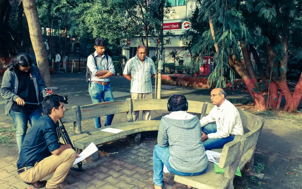 Crew and interviewee on a curved bench in a neighbourhood garden