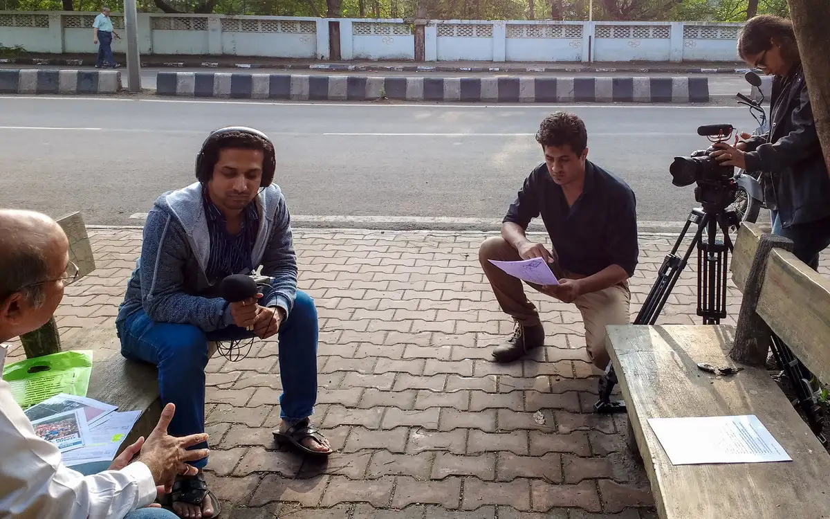 Interview being filmed on a footpath bench beside a city road