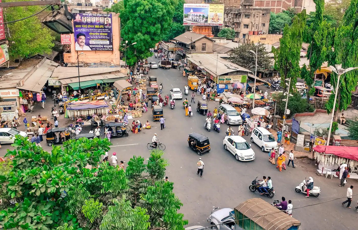 A crowded market junction seen from above, with cars, autorickshaws, two wheelers and pedestrians sharing the road