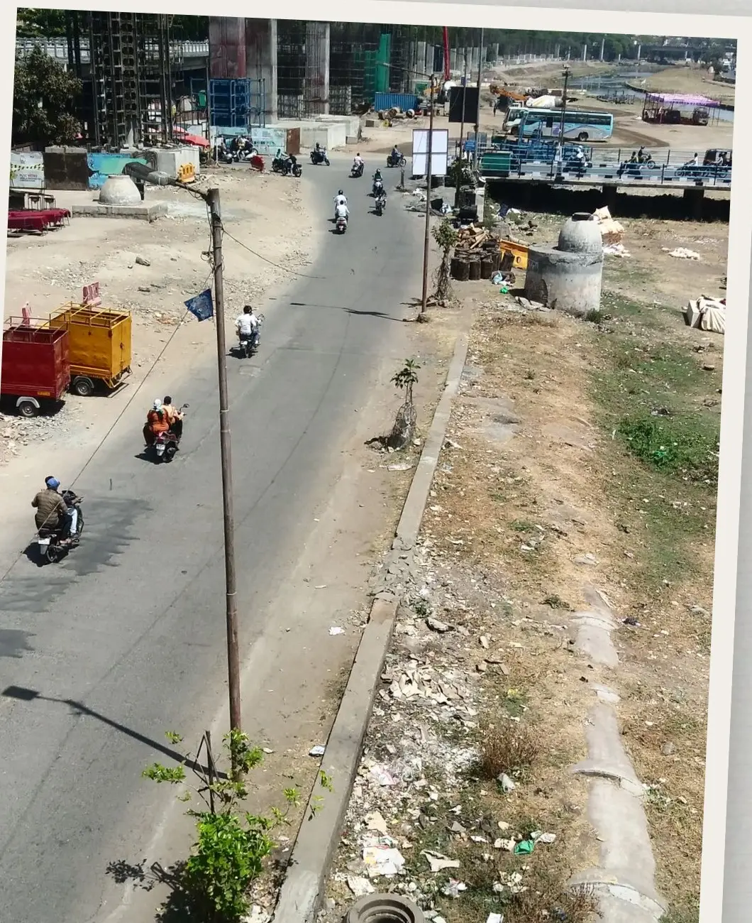 A wide road cutting past open ground on the edge of Pune, with traffic and dumped rubble